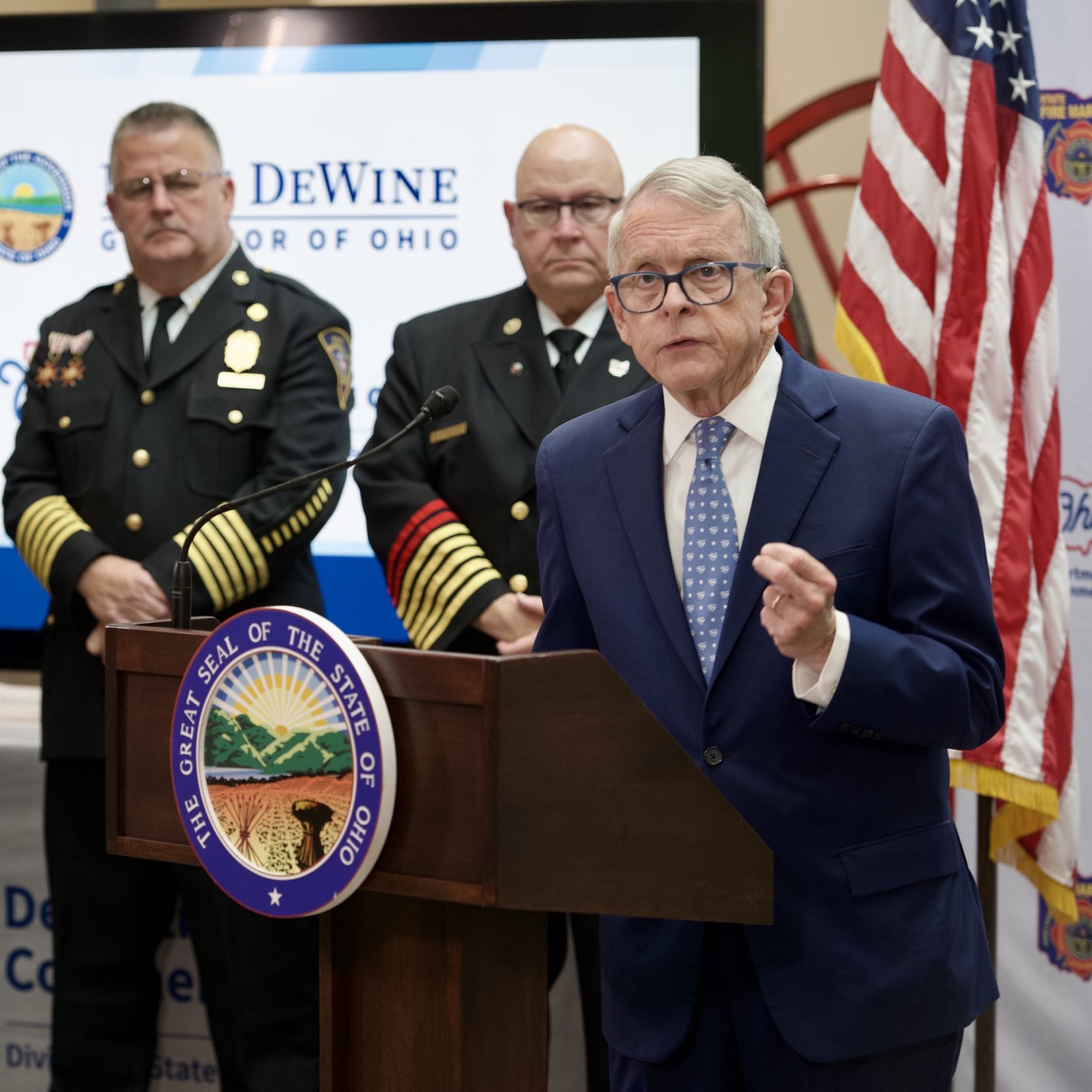 DeWine speaking at podium infront of informed officers and American flag.